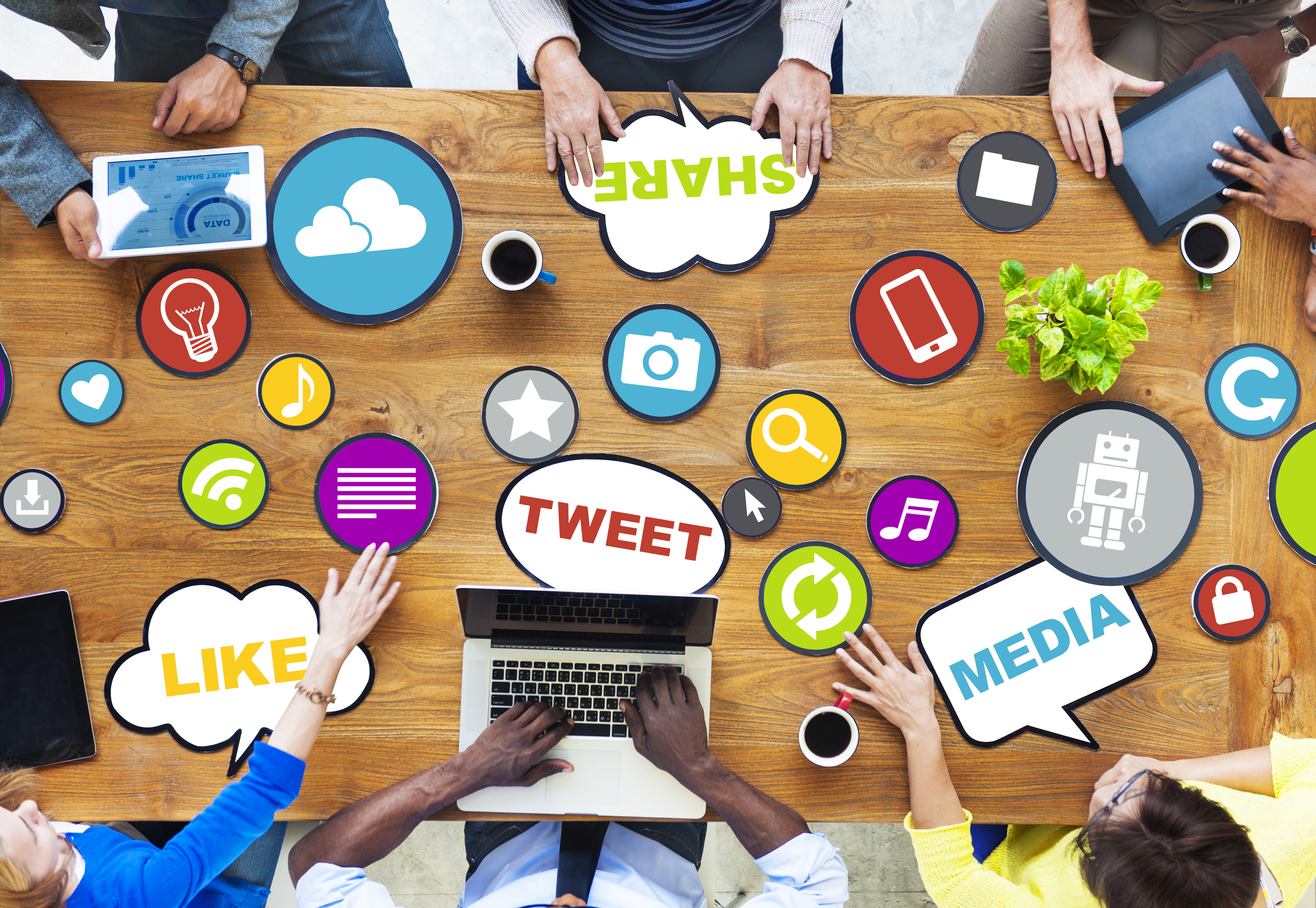 Bird's eye view of people seated at a table for a meeting. On the table there are many different icons that are associated with social media 